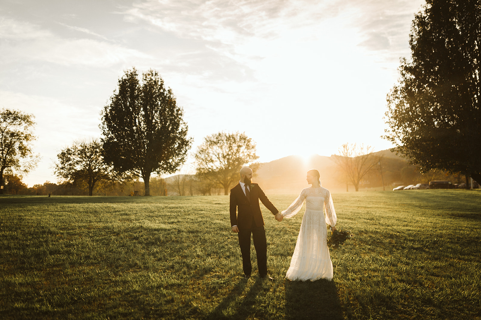 Golden hour light shins behind the bride and groom as they stand apart and hold hands at the Tennessee Riverplace