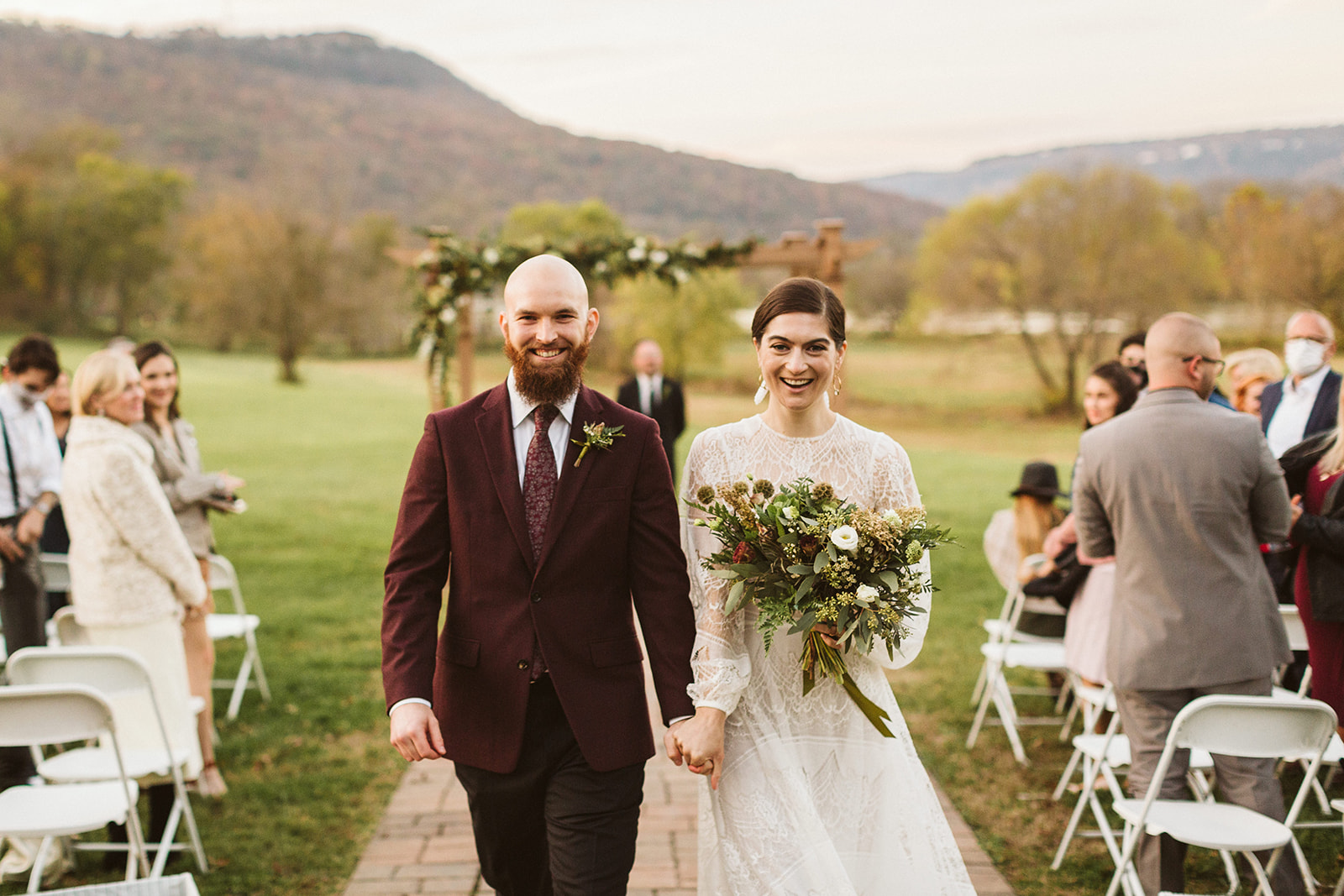 Bride and groom hold hands and smile as they walk down the aisle at their wedding in the Tennessee Riverplace