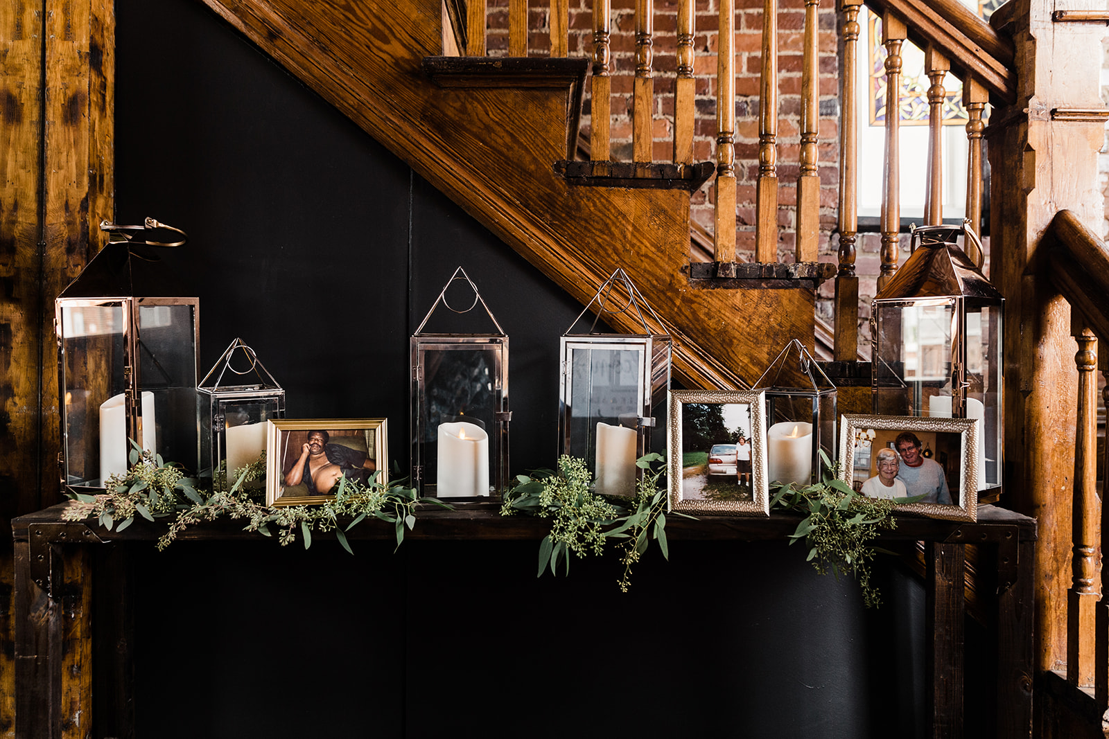 A welcome table at a wedding featuring candles, greenery, and photos of past family members.