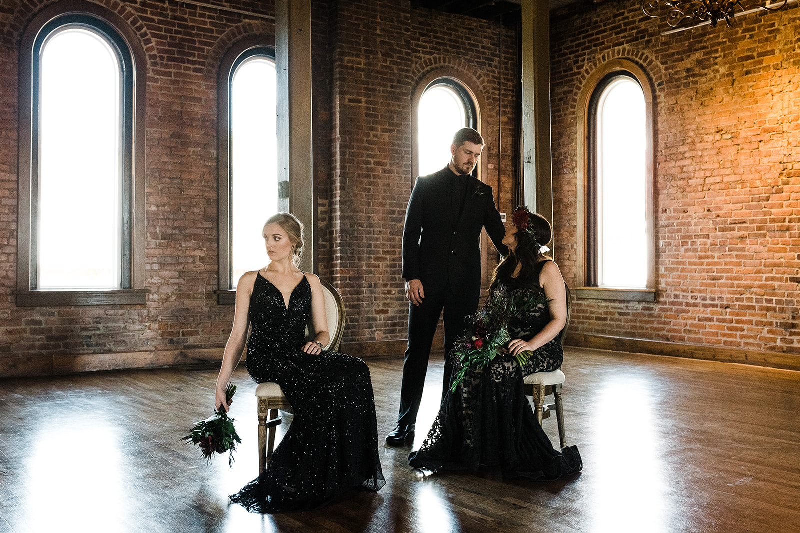 Bridal party members pose in black dresses in front of a wall of exposed brick.