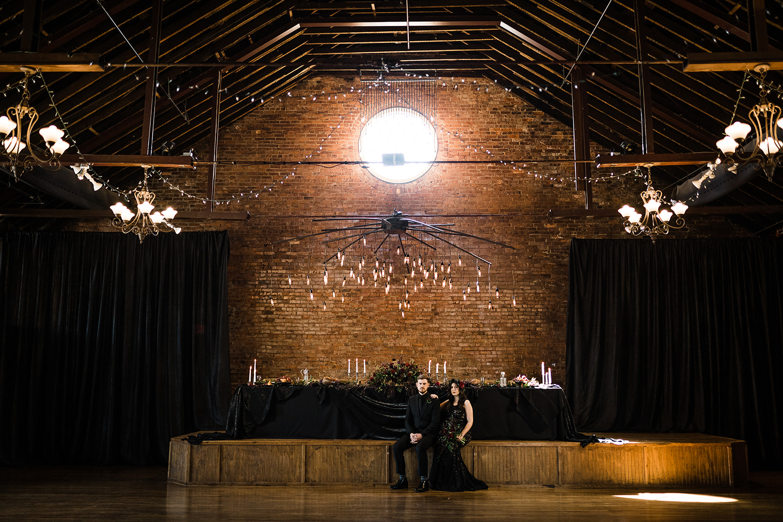 A bride and groom sit in front of their gothic head table at their modern, industrial wedding venue.