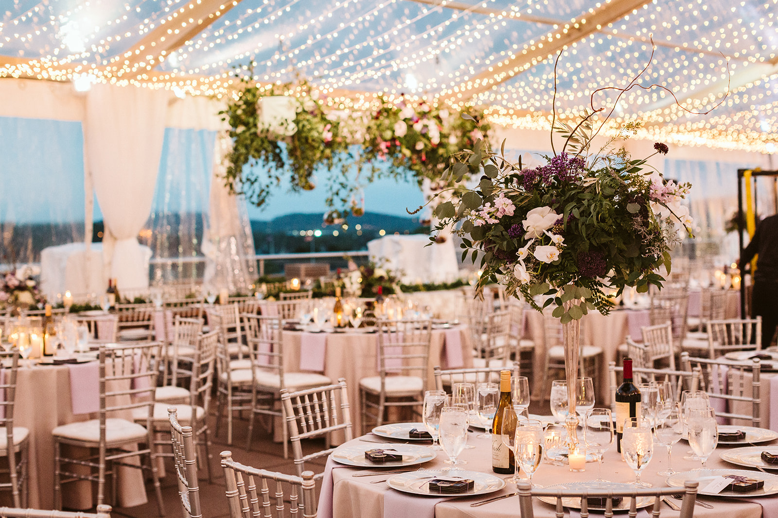 An outdoor wedding reception space decorated with fairy lights and greenery.