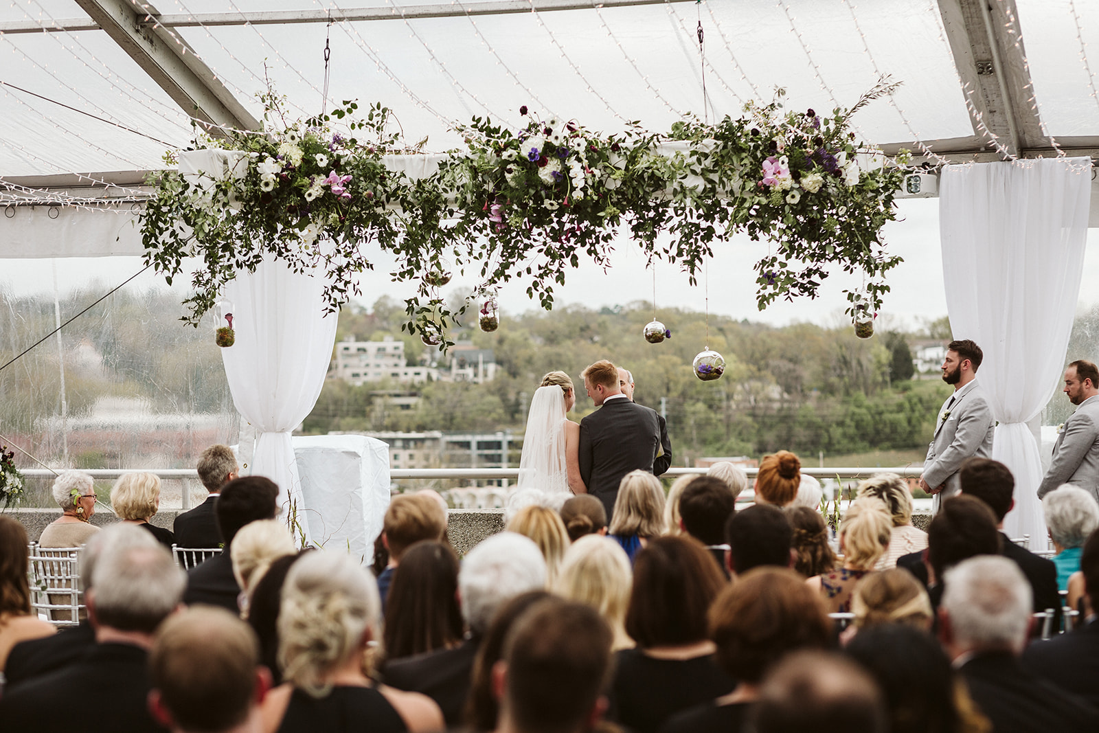 Bride and groom exchange vows beneath a hanging floral arrangement.