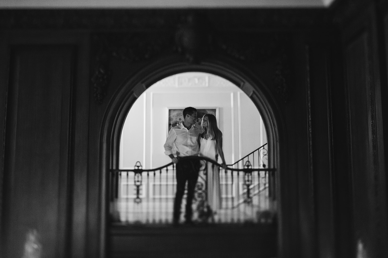 A bride and groom pose together in an archway on the landing of an old staircase.