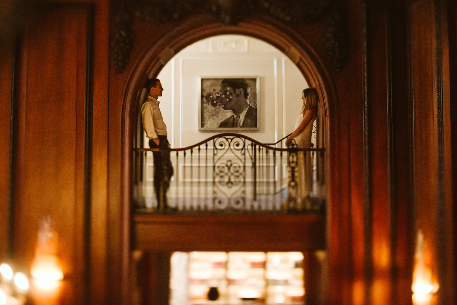 A bride and groom pose together in an archway on the landing of an old staircase.