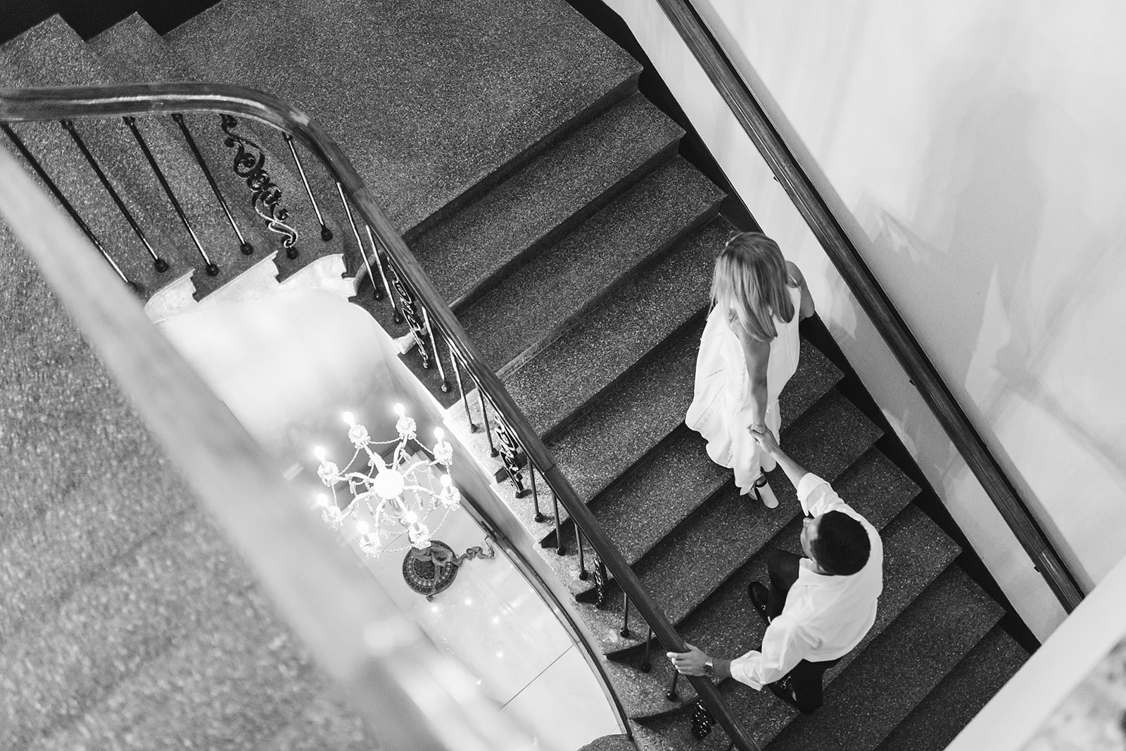 Overhead shot of a bride leading a groom up a winding staircase.
