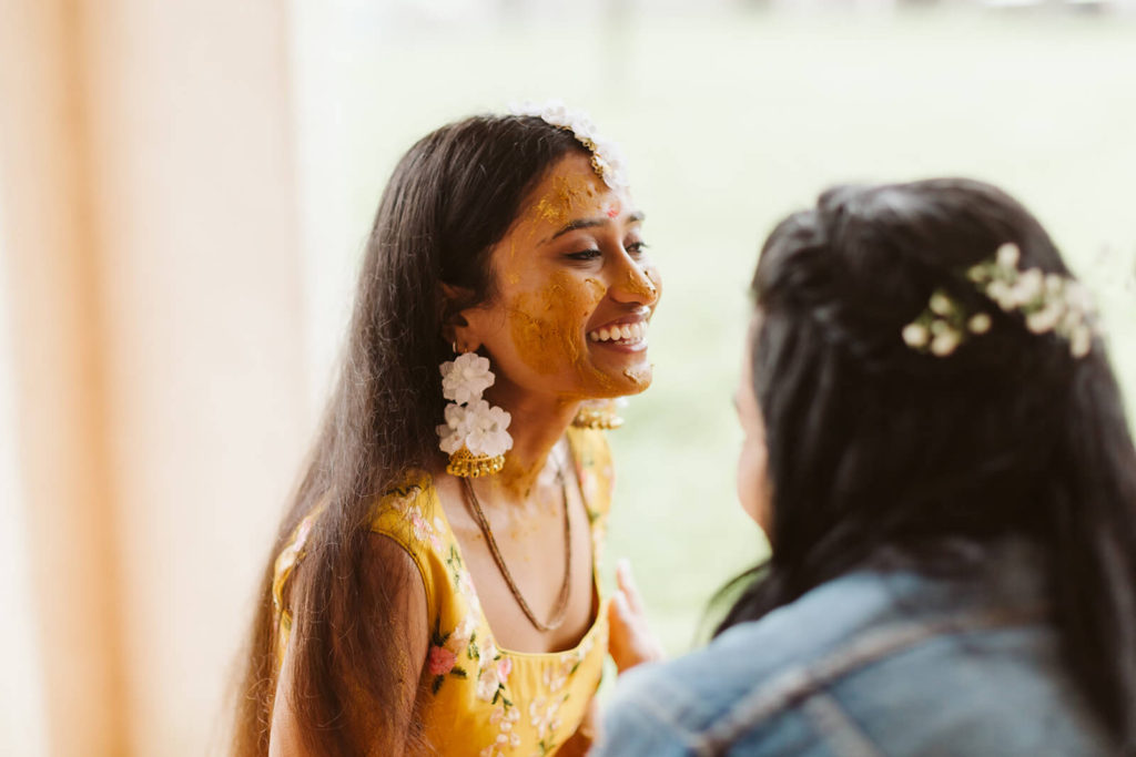 Smiling bride during Pithi ceremony of an Indian wedding. Photo by OkCrowe Photography.