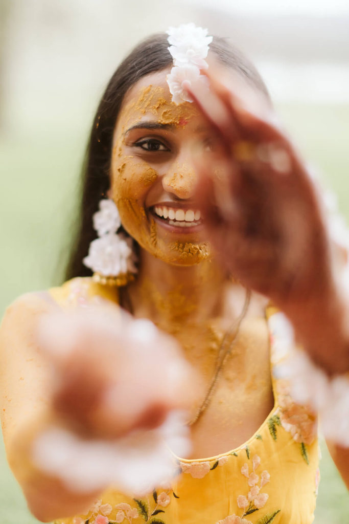 Bride wearing a yellow floral dress with tumeric paste on her face for Pithi ceremony. Photo by OkCrowe Photography.