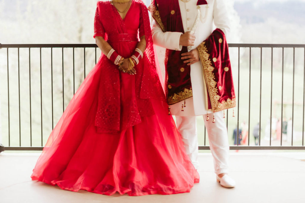 Bride's traditional red wedding dress and groom's white sherwani and red stole. Photo by OkCrowe Photography.