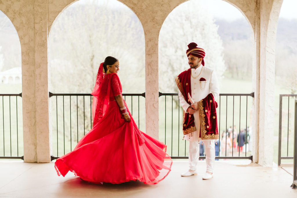 Bride showing off her red wedding dress to her groom on a balcony. Photo by OkCrowe Photography.