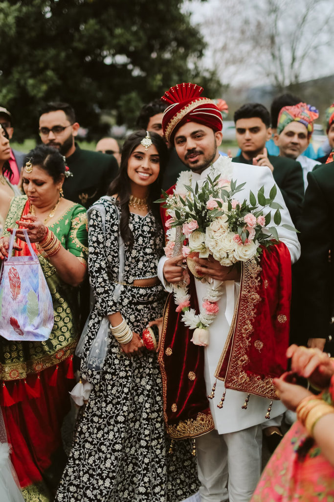 Indian groom posing with a wedding guest wearing a black and white sari. Photo by OkCrowe Photography.