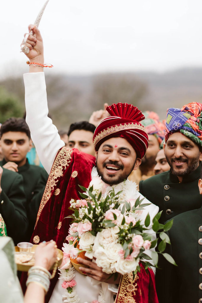 Indian groom holding a ceremonial knife and bouquet during an Indian wedding. Photo by OkCrowe Photography.