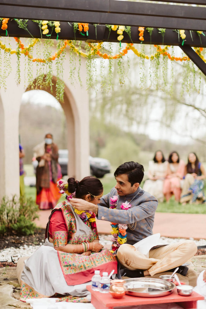 Placing a flower garland over the bride's head during the Vidhi ceremony. Photo by OkCrowe Photography.