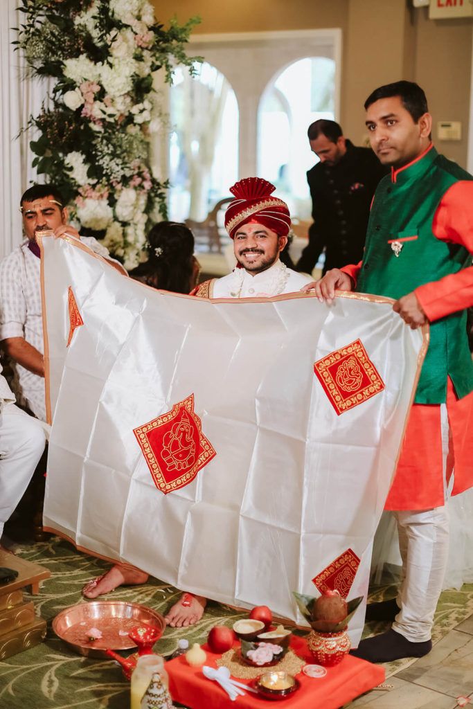 Indian groom hiding behind a shawl during a traditional wedding ceremony. Photo by OkCrowe Photography.