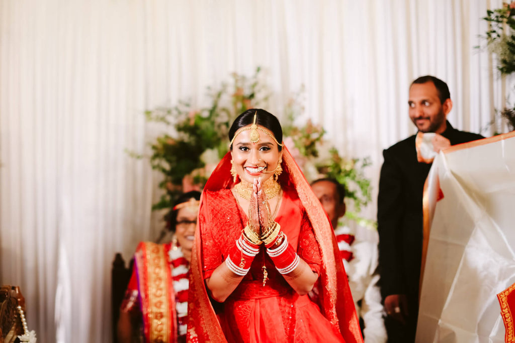 Indian bride wearing a traditional red wedding dress with her hands folded together. Photo by OkCrowe Photography.