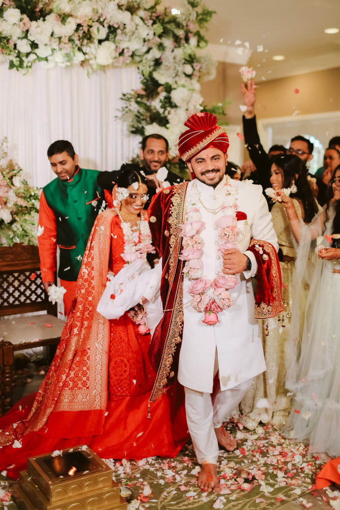 South Asian bride and groom being showered with white rose petals by wedding guests. Photo by OkCrowe Photography.