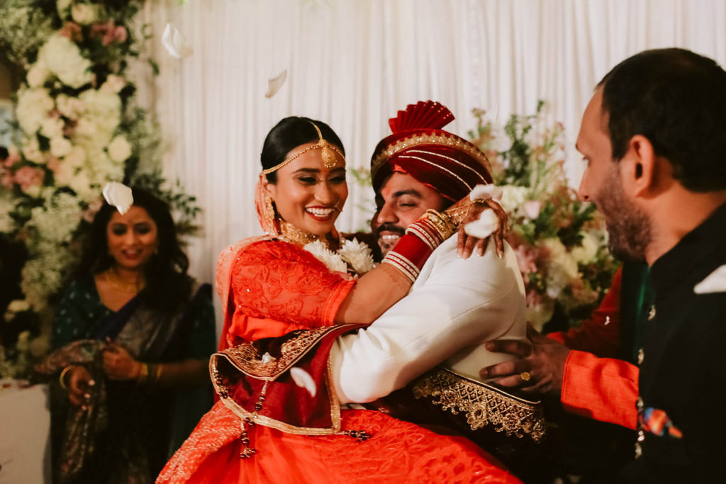 Indian bride and groom in traditional wedding ceremony with petals being thrown over them. Photo by OkCrowe Photography.