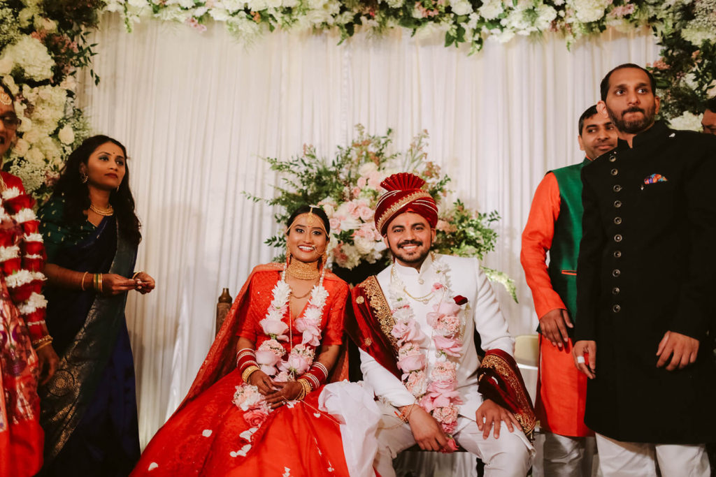 Bride and groom seated at the altar of their South Asian wedding ceremony with wedding guests around them. Photo by OkCrowe Photography.