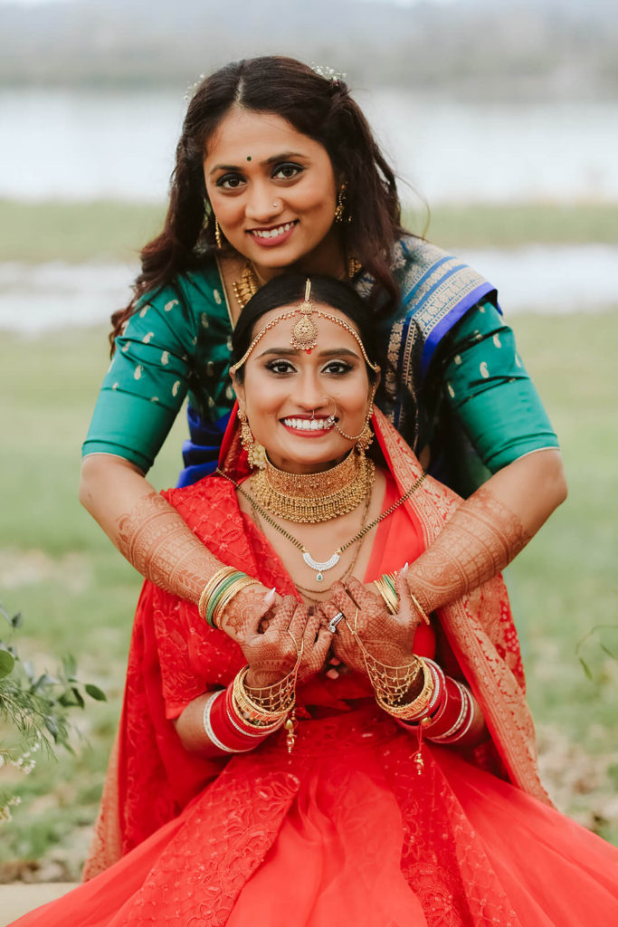 Indian bride wearing traditional red wedding dress with her sister. Photo by OkCrowe Photography.