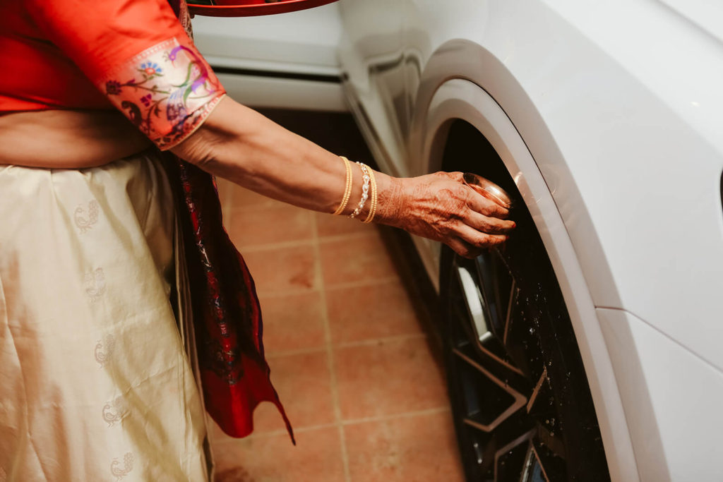 Indian wedding guest blessing bride and groom's car with perfumed water. Photo by OkCrowe Photography.