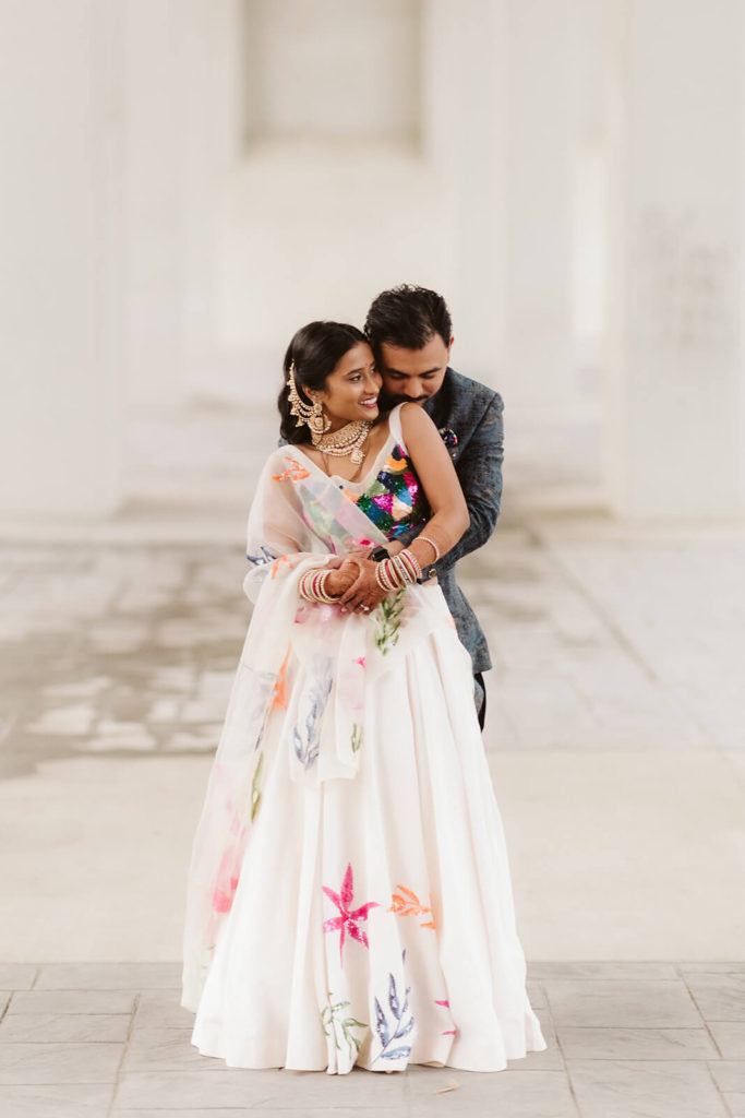 Bride and groom embracing wearing South Asian wedding garments. Photo by OkCrowe Photography.