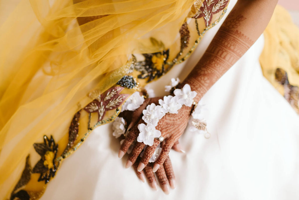 Hands covered in henna over yellow and white wedding dress. Photo by OkCrowe Photography.