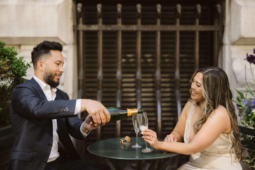 A couple sharing a champagne toast in Bryant Park during their engagement session. Photo by OkCrowe Photography. 