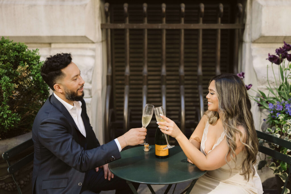 A couple sharing a champagne toast in Bryant Park during their engagement session. Photo by OkCrowe Photography. 