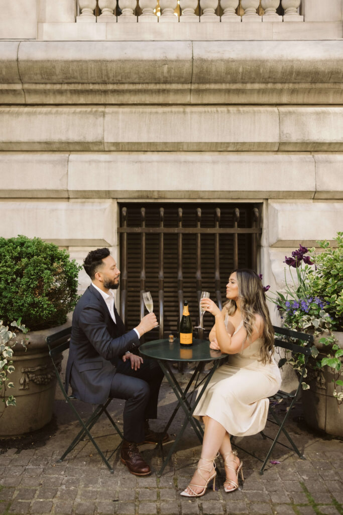 A couple sharing a champagne toast in Bryant Park during their engagement session. Photo by OkCrowe Photography. 