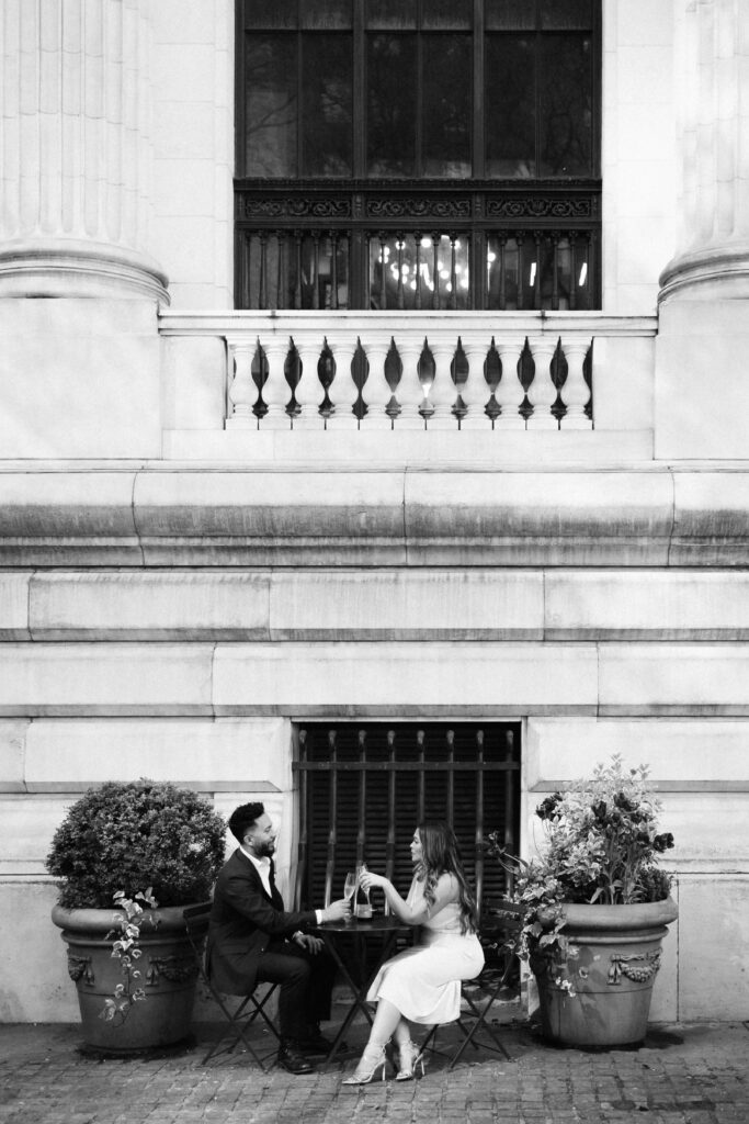 A couple sharing a champagne toast in Bryant Park during their engagement session. Photo by OkCrowe Photography. 