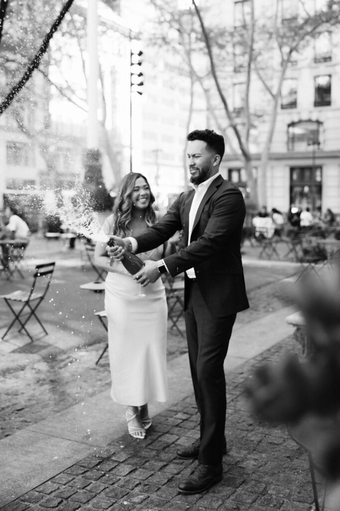 A couple sharing a champagne toast in Bryant Park during their engagement session. Photo by OkCrowe Photography. 