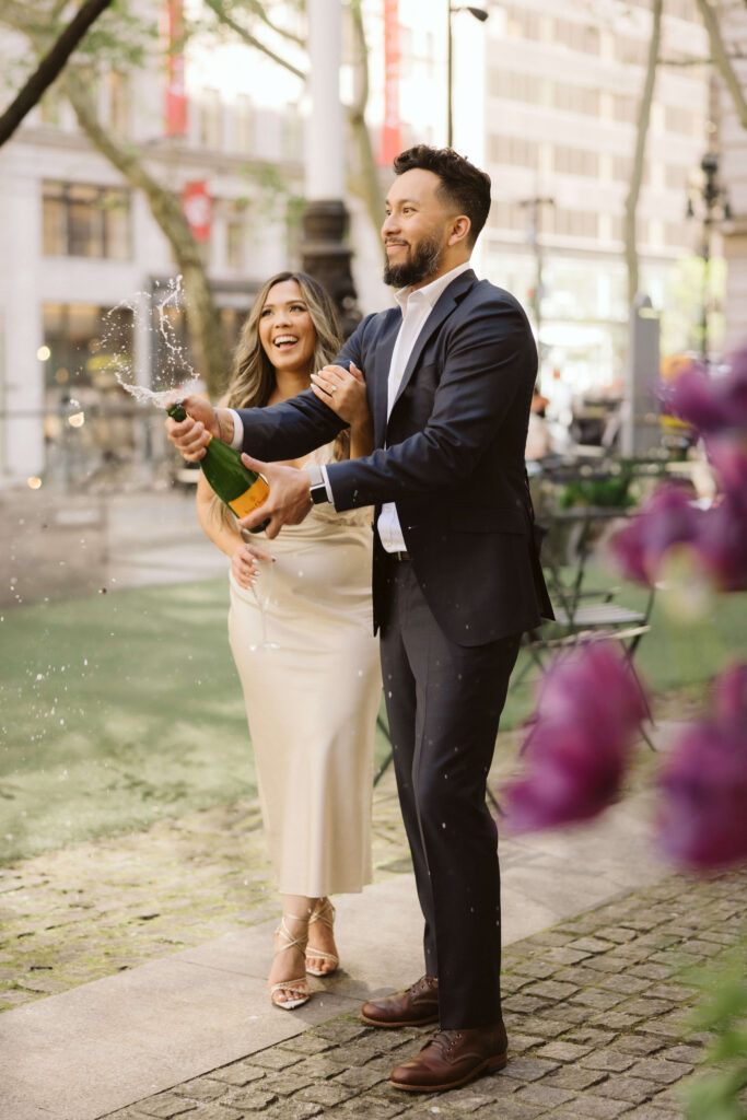 A couple sharing a champagne toast in Bryant Park during their engagement session. Photo by OkCrowe Photography. 