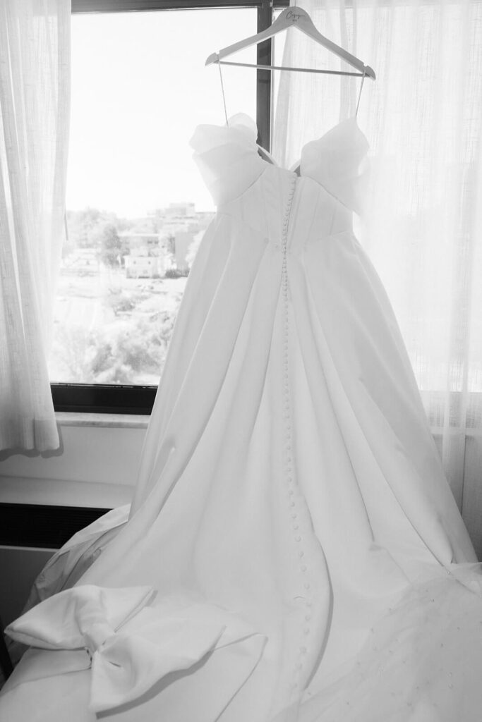 Bride's wedding dress hanging by a window. Photo by OkCrowe Photography.